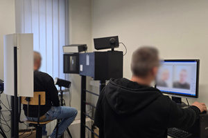 Nieumundurowany policjant - technik kryminalistyki wykonuje zdjęcie sygnalityczne zatrzymanego mężczyzny.