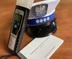 Policyjna czapka z białym otokiem, urządzenie do badania stanu trzeźwości i bloczek mandatowy.