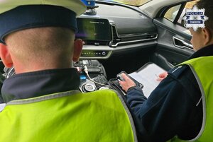 Dwaj policjanci wewnątrz radiowozu. Jeden z nich sporządza dokumentację.