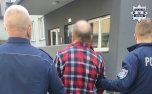Policjanci prowadzą zatrzymanego mężczyznę.