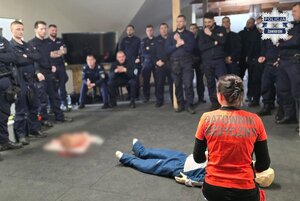 Policjanci obserwują ratowniczkę medyczną, klęczącą przy fantomie.