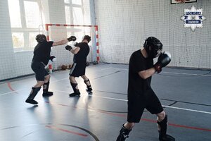 Nieumundurowani policjanci, w kaskach ochronnych, ćwiczą na sali gimnastycznej.