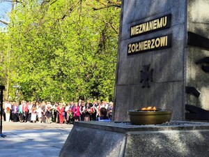Częściowo widoczny pomnik Nieznanego Żołnierza oraz palący się na nim znicz. W tle zgromadzone na uroczystości osoby.