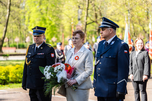 Delegacja z kwiatami podchodząca do pomnika. Wśród delegatów policjant.