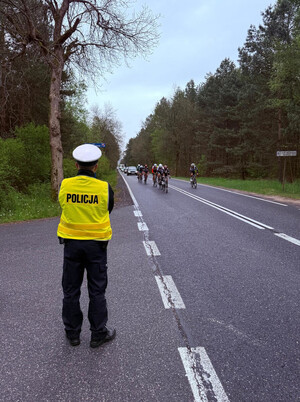 Policjant wydziału ruchu drogowego obserwujący drogę, po której jadą kolarze.