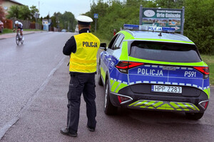 Policjant wydziału ruchu drogowego obserwujący drogę, po której jadą kolarze.