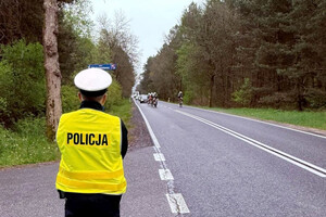 Policjant wydziału ruchu drogowego obserwujący drogę, po której jadą kolarze.