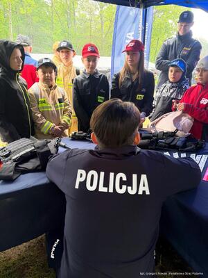 Policjant rozmawia z osobami obecnymi przy stoisku profilaktycznym. Zdjęcie: kapitan Grzegorz Nowak. Powiatowa Państwowa Straż Pożarna w Zawierciu.