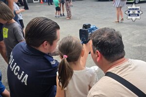 Policjant prezentuje sprzęt drogówki dziewczynce i jej opiekunowi.