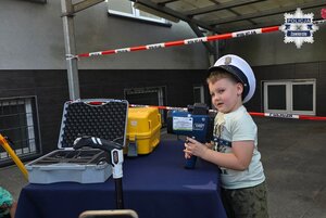 Chłopiec w czapce policjanta ruchu drogowego trzyma w dłoniach miernik prędkości.