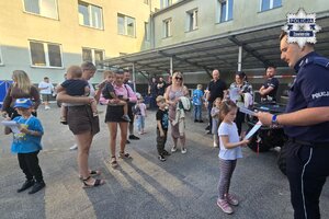 Policjant rozdaj dyplomy. Widoczne dzieci wraz z opiekunami.