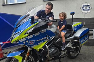 Chłopiec siedzi na policyjnym motocyklu. Obok niego stoi policjant.