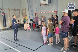 Policjant wraz z dziećmi i opiekunami na sali gimnastycznej.