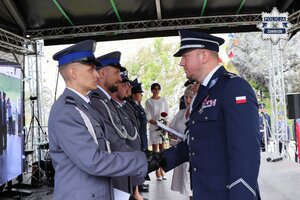 Komendant Powiatowy Policji w Zawierciu młodszy inspektor Renata Hałabuda, obok której obecny jest Pierwszy Zastępca Komendanta Wojewódzkiego Policji w Katowicach inspektor Radosław Kacprzak, wręcza policjantowi akt mianowania.