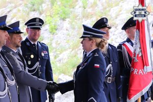 Komendant Powiatowy Policji w Zawierciu młodszy inspektor Renata Hałabuda gratuluje policjantowi. Obok widoczny Pierwszy Zastępca Komendanta Wojewódzkiego Policji w Katowicach inspektor Radosław Kacprzak.