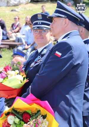 Komendant Powiatowy Policji w Zawierciu młodszy inspektor Renata Hałabuda wraz ze swoim zastępcą podinspektorem Pawłem Sobotą trzymają bukiety kwiatów.