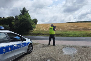 Policjant dokonuje pomiaru prędkości. Widoczny także zaparkowany radiowóz.