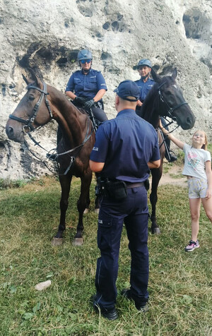 Policjantki na koniach, przed którymi stoi policjant. obok dziewczynka głaska jednego z koni.